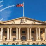 Front view of the Bank of England building in London under a clear blue sky, with the Union Jack flag flying atop the central pediment.