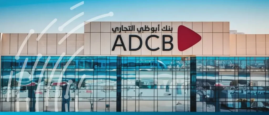Exterior view of an ADCB (Abu Dhabi Commercial Bank) building featuring the bank's logo in English and Arabic against a blue sky, with a stylized digital wave graphic overlaid on the left.