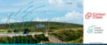 A landscape of wind turbines on a green hillside under a blue sky, featuring CarbonChain and Trade Finance Global logos to announce the launch of the CarbonChain Comply platform.