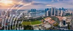 An aerial, panoramic view of the Singapore city skyline at sunset. The image features the Marina Bay Sands resort and the downtown financial district with numerous skyscrapers. The sky is a warm blend of orange and purple. Overlaid on the left side are stylized, white curved data lines and dots suggesting connectivity or energy flow. A solid teal bar runs across the very bottom of the image.