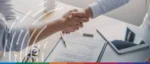 Close-up of a professional handshake over a signed contract and digital tablet, representing the SBA enhancing Surety Bond Guarantee limits for small businesses.