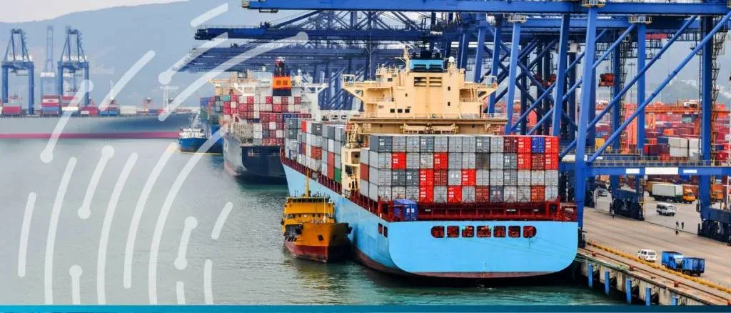 A busy commercial shipping port with multiple large container ships docked under industrial blue cranes, representing the stability of global supply chains after the US dock workers' strike.