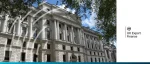 The grand white stone facade of the UK HM Treasury building in London under a blue sky.